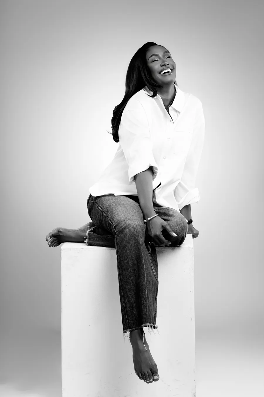 Awa Mballo Tall riant, en chemise blanche et jean, assise